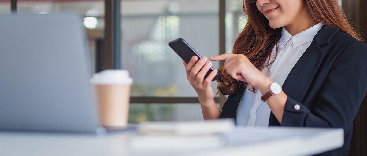 Frau sitzt an einem Tisch mit Handy in der Hand 